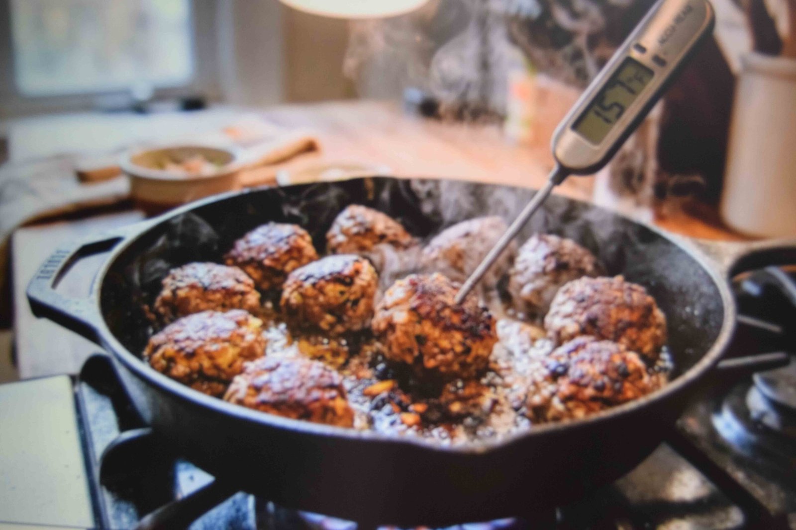 Chicken meatballs browning in a skillet with a thermometer checking the centre