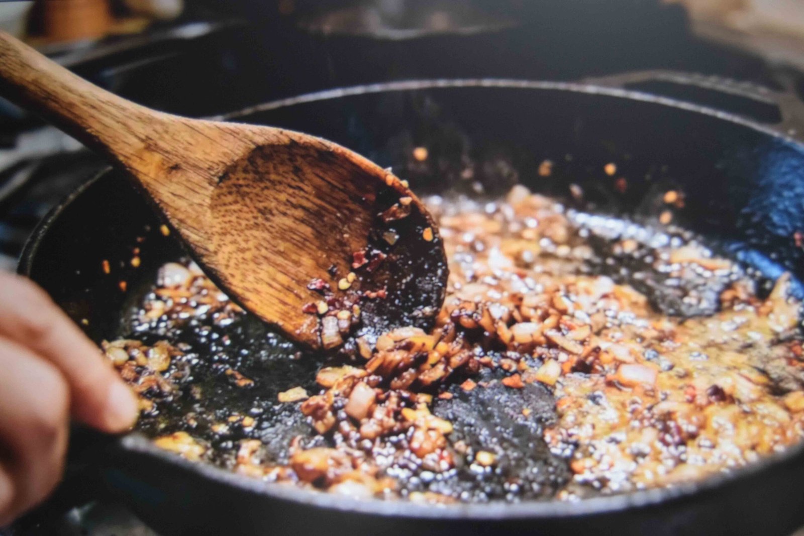 A wooden spoon lifting browned bits while shallot and garlic cook