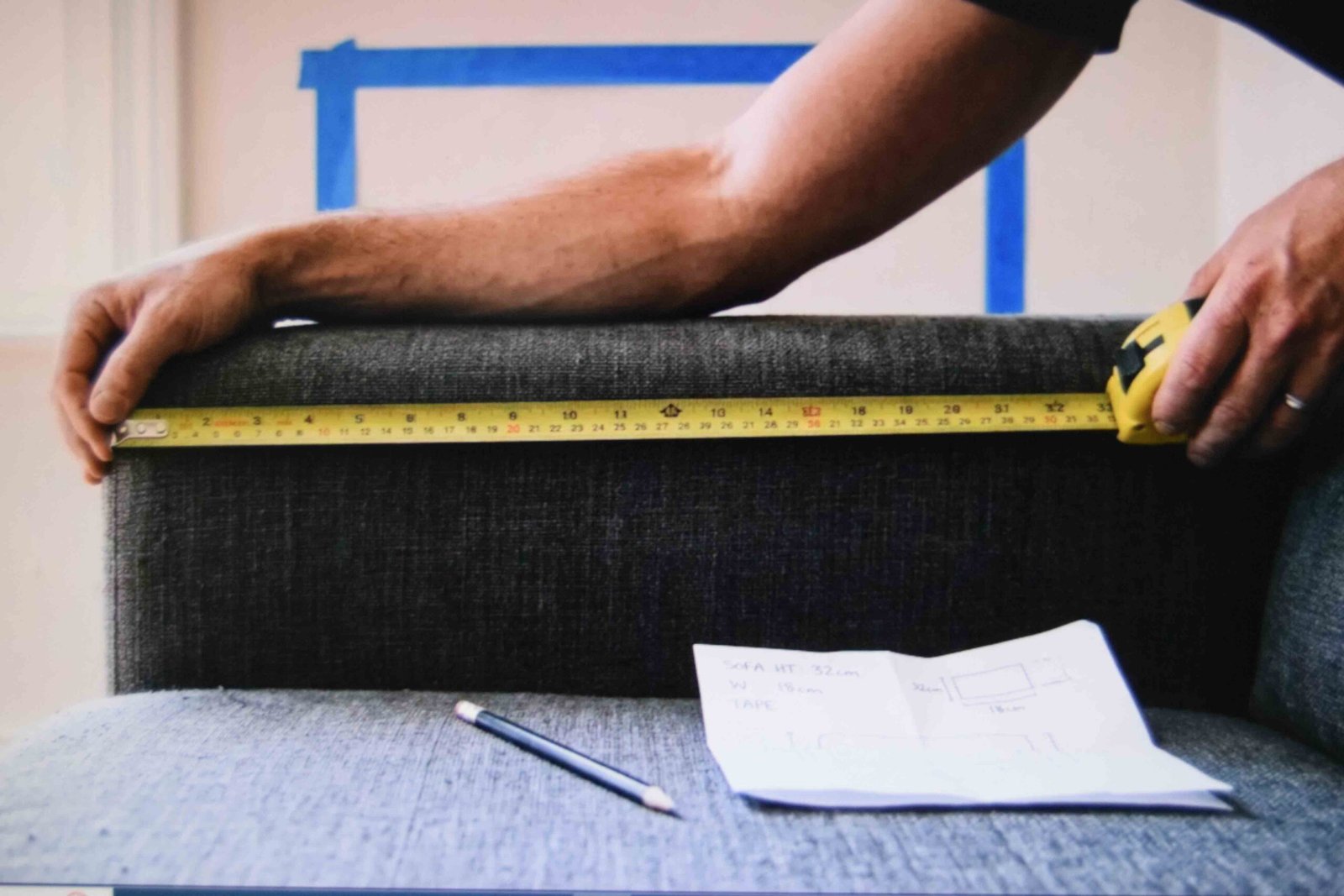 A tape measure stretched across a sofa back with a paper template taped to the wall