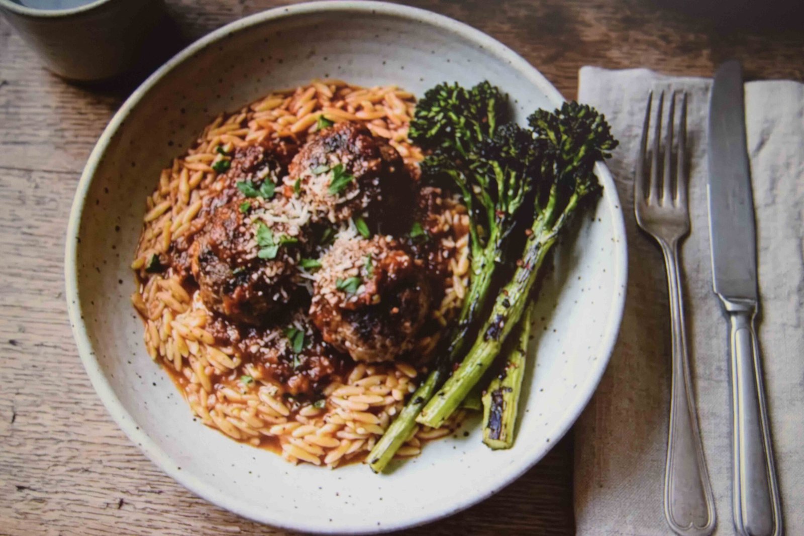 Orzo topped with chicken meatballs and sauce served with charred broccolini